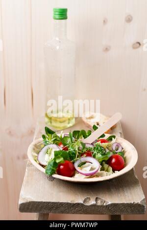 Vegan Salat (einkorn Weizen, Tomaten, Feldsalat, rote Zwiebel Ringe, Eisbergsalat, Kresse, schwarzer Pfeffer) in ein Palmblatt Schale Stockfoto