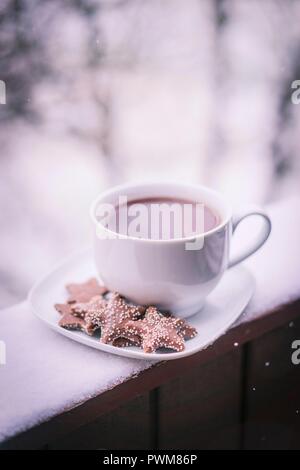 Eine heiße Tasse Tee mit Keksen auf einer Untertasse auf einem Verschneiten Balkon Stockfoto