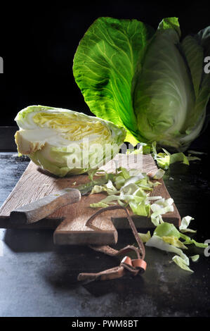 Spitzkohl, ganz, halbiert und in Scheiben geschnitten, auf einem Schneidebrett mit Messer auf einem schwarzen Backblech Stockfoto