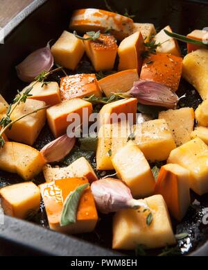 Rohe Kürbis Stücke mit Knoblauch, Salbei und Thymian in eine Bratenform Fach Stockfoto