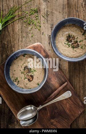 Zwei Schalen mit dicken und cremige Pilzsuppe garniert mit Pilz Schichten und Schnittlauch in blau Schalen auf einem hölzernen Oberfläche Stockfoto