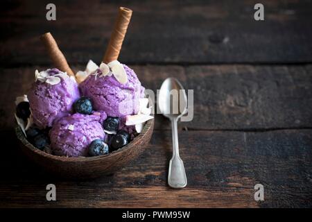 Kugeln Heidelbeere Eis gekrönt mit gehobelten Mandeln und Schokolade Waffelröllchen in eine hölzerne Schüssel Stockfoto