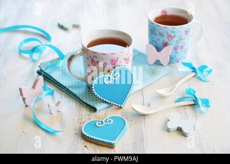 Herzförmige Kekse dekoriert mit blauen und weißen Sahnehäubchen serviert mit zwei Tassen Kaffee Stockfoto