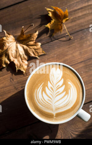 Flache weiße, Cappuccino mit Rosetta oder florette Latte Art auf einer hölzernen Hintergrund mit Blätter im Herbst Stockfoto
