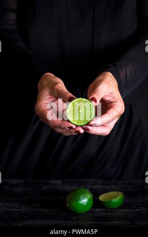 Eine halbe Limette in die Hände einer Frau vor einem schwarzen Hintergrund Stockfoto