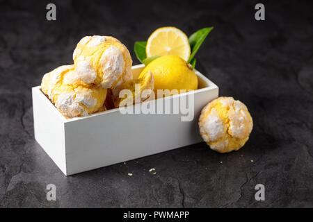 Hausgemachte Zitrone crinkle Plätzchen mit Puderzucker in kleinen weißen Kasten, auf dunklem Hintergrund Stockfoto