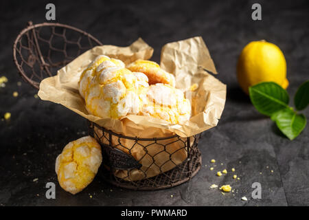 Hausgemachte Zitrone crinkle Plätzchen mit Puderzucker Puderzucker auf Trägerpapier in kleinen Metall, auf dunklem Hintergrund Stockfoto