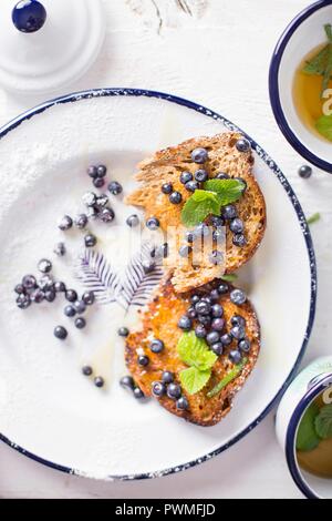 Toast mit Blaubeeren, Minze und Honig auf einem weißen Teller serviert Stockfoto