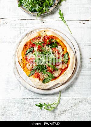 Dünne Kruste Pizza mit Spinat, Salami und Gorgonzola überbacken mit frischem Rucola Stockfoto