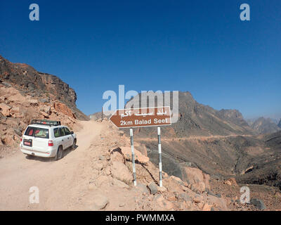 Oman, Wadi Bani Awf, ein Allradantrieb weiße landcruiser an einem Feldweg vor dem Schild des Dorfes Bilad sayt in der Mitte von einem wüstenklima Landschaft Stockfoto