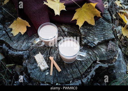 Tassen Kakao und Snacks auf natürliche Holz Hintergrund mit Blätter im Herbst. Milch Kaffee im Glas Tassen auf schöne strukturierte Holzoberfläche im Freien Stockfoto