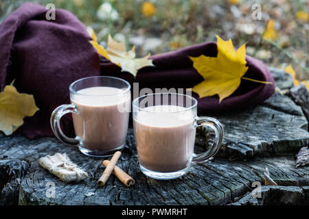 Milch Kaffee im Glas Tassen auf schöne strukturierte Holzoberfläche im Freien. Tassen Kakao auf die natürlichen Holz Hintergrund mit Blätter im Herbst. Stockfoto