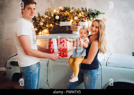 Blick auf schöne Daddy, Weihnachtsgeschenk, Big Red Box, für blonde Mutter und kleinen niedlichen Tochter. Familie Ausgabe Zeit zusammen im Haus eingerichtet w Stockfoto