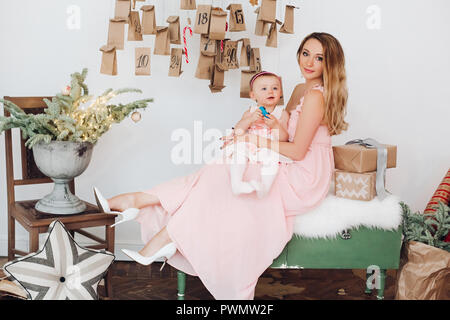 Schöne Mama mit Tochter in rosa Kleider spielen in der Nähe von Weihnachten Dekoration. Stockfoto