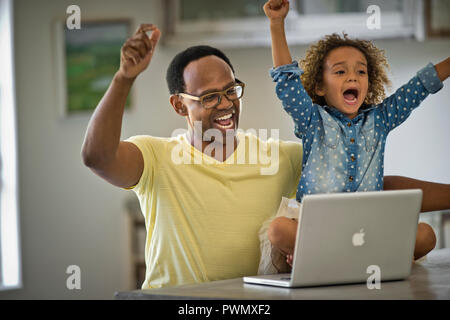 Vater und Tochter zujubeln, während der Computer verwendet wird. Stockfoto