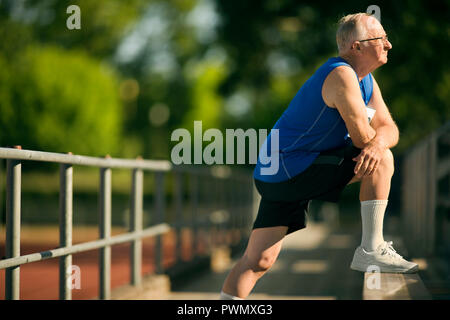 Älterer mann Aufwärmen mit erstreckt sich auf zuschauertribünen. Stockfoto