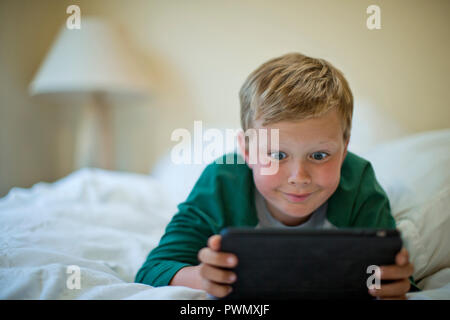 Junge ziehen ein dummes Gesicht beim Spielen mit einem digitalen Tablet. Stockfoto