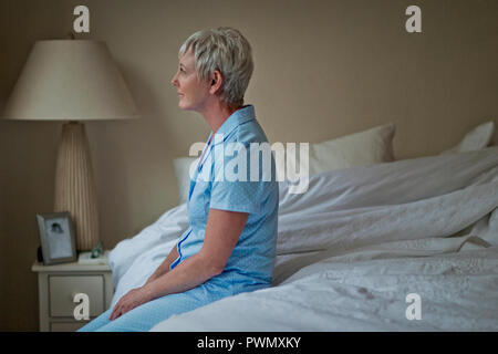 Reife Frau sitzt in ruhiger Lage am Rande von ihrem Bett und hat ein Moment der Reflexion vor Beginn des Tages. Stockfoto