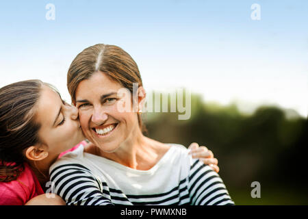 Junge Mädchen küssen sie lächelnd Mutter auf die Wange. Stockfoto