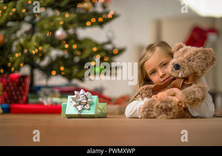 Porträt eines jungen Mädchens ihr Teddybär auf Weihnachten Morgen umarmt. Stockfoto