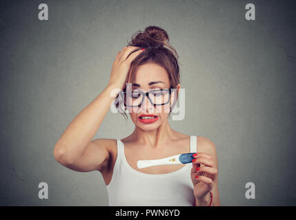 Portrait einer jungen Frau schockiert mit positiven Schwangerschaftstest Stockfoto