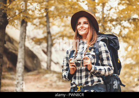 Glückliche junge Frau mit Rucksack tragen braunen Hut, Plaid Shirt, Jeans und braune Stiefel wandern mit Trekking Stöcke, mit Blick auf die wundervollen Felsen und immer bereit zu Fotografieren, Reisen Konzept Stockfoto