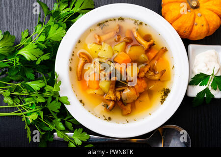 Herbst chanterelle Pilzsuppe mit Huhn, Kürbis, saure Sahne, Lorbeerblatt, Kürbis, Petersilie in einer weißen Schüssel, Löffel, schwarzen Hintergrund. Ansicht von Oben. Stockfoto