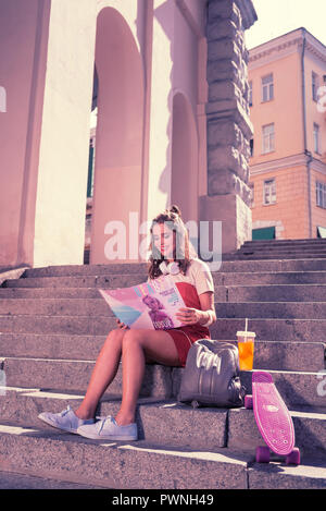 Strahlende junge Frau ihr Wochenende genießen mit Magazin und Sommer cocktail Stockfoto