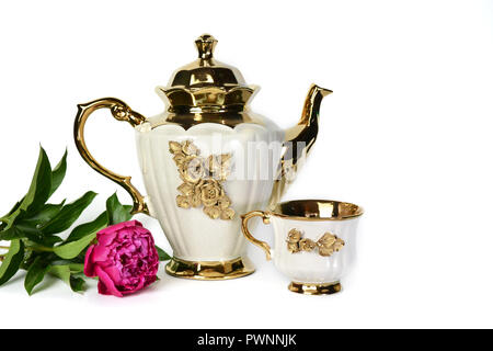 Eine Weisse Teekanne mit einer Goldenen Blume, einem milchkännchen, einer Tasse Tee und einem schönen lila Pfingstrose. Stockfoto