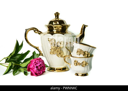 Eine Weisse Teekanne mit einer Goldenen Blume, eine Tasse Tee und ein schönes lila Pfingstrose. Stockfoto