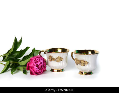 Zwei weiße Tassen mit einem goldenen Griff und eine Blume. Stockfoto