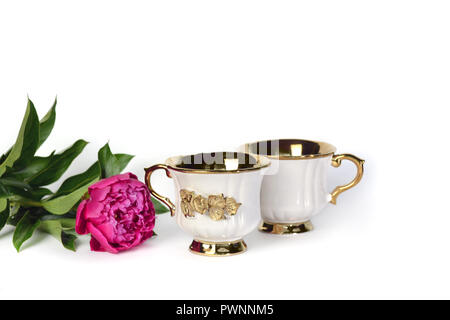 Zwei weiße Tassen mit einem goldenen Griff und eine Blume. Stockfoto