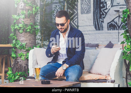 Geschäftsmann mit der Eingabe auf seinem Smartphone im Cafe. Flasche Bier auf den Tisch. Stockfoto