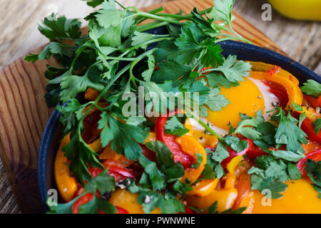 Shakshuka, Spiegelei, Tomaten und Paprika Sauce aus Gusseisen Skillet auf rustikalen Holztisch gekocht Stockfoto
