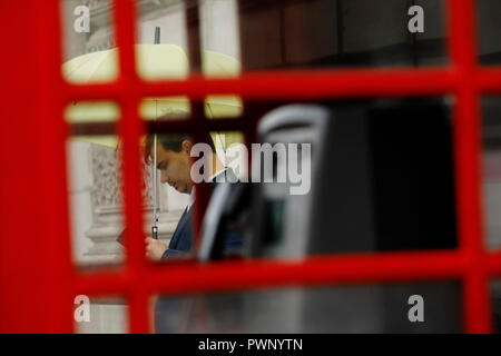 London, Großbritannien. 17. Okt 2018. UK Wetter: ein Mann hält einen yellow umbrella außerhalb einer traditionellen roten Telefonzelle bei herbstlichen Wetter im Whitehall in London, Mittwoch, 17. Oktober 2018. Foto: © Lukas MacGregor Credit: Lukas MacGregor/Alamy leben Nachrichten Stockfoto