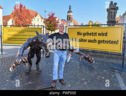 17 Oktober 2018, Brandenburg, Cottbus: Rainer Opolka, Künstler und Unternehmer, steht auf dem Altmarkt neben einem bronze Wolf. Der Bildhauer Opolka will gegen Gewalt und Hass mit einer Mahnwache auf dem Altmarkt in Cottbus zu demonstrieren. Am Mittwoch, den vier Bronze wolf Skulpturen und Informationstafeln errichtet wurden auf dem zentralen Platz im Zentrum der Stadt. Die Mahnwache in Cottbus gerichtet Opolka gegen was er als zunehmende Radikalisierung in der AfD. Die Partei ist unter Druck, weil die Bundesländer "Amt für den Schutz der Verfassung ist Material sammeln, um Whe zu entscheiden, Stockfoto