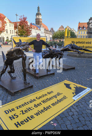 17 Oktober 2018, Brandenburg, Cottbus: Rainer Opolka, Künstler und Unternehmer, steht auf dem Altmarkt unter bronze Wölfe. Der Bildhauer Opolka will gegen Gewalt und Hass mit einer Mahnwache auf dem Altmarkt in Cottbus zu demonstrieren. Am Mittwoch, den vier Bronze wolf Skulpturen und Informationstafeln errichtet wurden auf dem zentralen Platz im Zentrum der Stadt. Die Mahnwache in Cottbus gerichtet Opolka gegen was er als zunehmende Radikalisierung in der AfD. Die Partei ist unter Druck, weil die Bundesländer "Amt für den Schutz der Verfassung ist Material sammeln, um auf den Geschmack entscheiden Stockfoto