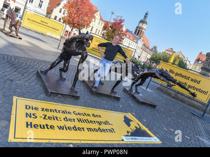 17 Oktober 2018, Brandenburg, Cottbus: Rainer Opolka, Künstler und Unternehmer, steht auf dem Altmarkt unter bronze Wölfe. Der Bildhauer Opolka will gegen Gewalt und Hass mit einer Mahnwache auf dem Altmarkt in Cottbus zu demonstrieren. Am Mittwoch, den vier Bronze wolf Skulpturen und Informationstafeln errichtet wurden auf dem zentralen Platz im Zentrum der Stadt. Die Mahnwache in Cottbus gerichtet Opolka gegen was er als zunehmende Radikalisierung in der AfD. Die Partei ist unter Druck, weil die Bundesländer "Amt für den Schutz der Verfassung ist Material sammeln, um auf den Geschmack entscheiden Stockfoto