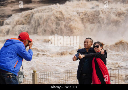 Yichuan, Shaanxi Chinas Provinz. 17 Okt, 2018. Touristen posieren für Fotos bei Hukou Wasserfall des Gelben Flusses in Yichuan County im Nordwesten der chinesischen Provinz Shaanxi, Okt. 17, 2018. Aufgrund der starken Niederschläge am Oberlauf des Gelben Flusses, das Wasservolumen des Hukou Wasserfall Überspannungen vor kurzem. Credit: Shao Rui/Xinhua/Alamy leben Nachrichten Stockfoto