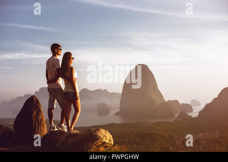 Ein junges Paar steht auf Big Rock und sieht bei Sonnenuntergang und Sonnenaufgang über dem Meer und Inseln Stockfoto