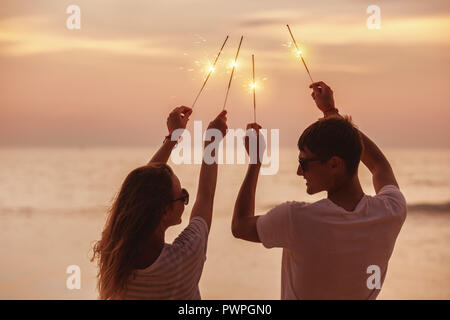 Glückliches Paar Spaß und feiert Sonnenuntergang mit Wunderkerzen in den Händen Stockfoto