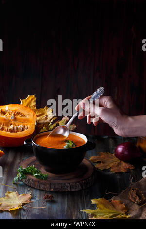 Weibliche hand rühren Kürbissuppe pürieren, mit grünen in eine Platte auf einen dunklen Tisch. Auf dem Hintergrund der Kürbisse Menü und Restaurant Konzept kopieren Raum Stockfoto