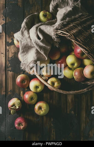 Reif im Garten Grün rote Äpfel in alten Korb mit Tuch über dunkle Plank Holz- Hintergrund. Flach, Platz. Herbst Ernte. Stockfoto