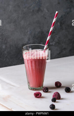 Glas Rote Früchte Beeren Wassermelone eisgekühlten Cocktail mit gestreiften Stroh und Gefrorene Beeren stehen auf weißem Marmor tisch mit grauen Wand im Hintergrund. Su Stockfoto