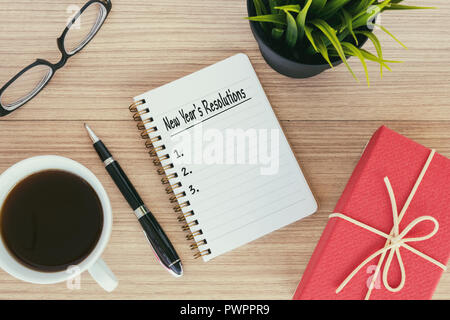 Beschlüsse des neuen Jahres Text in Notepad - Geschenkbox, Brillen, Kaffee, Stift, Topfpflanze. Stockfoto