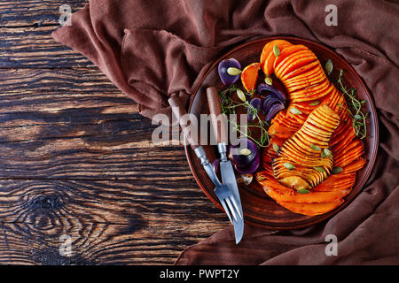 Gebratene Hälften der Butternut Squash oder Kürbis mit roten Zwiebeln, Thymian, Kürbiskerne und Gewürze auf einem Steingut Teller auf einem alten rustikalen Tisch in Scheiben geschnitten, vi Stockfoto