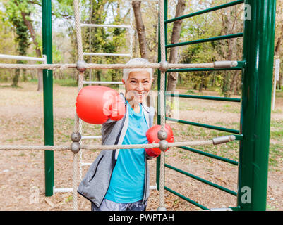Portrait von Happy Passen ältere Frau mit Boxhandschuh im Fitnessbereich im Freien in Sportbekleidung. Aktive alte Menschen Fitness Lifestyle Stockfoto