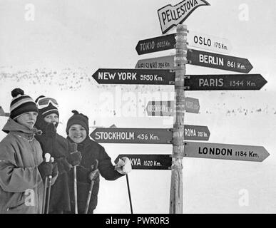 Winter in den 60er Jahren. Eine Gruppe junger Skifahrer steht vor der Zeichen, bei denen der Abstand zu den Städten wie New York und London in Km aufgeführt sind. Schweden 1967 Stockfoto