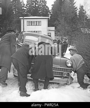 Winterfahren in den 1950er Jahren Ein Auto ist von der verschneiten Straße heruntergeschleudert und sitzt neben der Straße im Schnee fest. Eine Gruppe von Leuten schiebt es wieder auf die Straße. Schweden 1949. Foto Kristoffersson Ref. AU109-5 Stockfoto