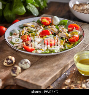 Leckere natürliche Salat mit fresly abgeholt grünes Gemüse, Hühnerfleisch, Wachteleier in einem grauen Platte mit Senfsauce auf einem Holztisch. Stockfoto